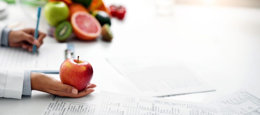 Doctor holding a fresh apple with diet plan and nutrition notes in the background, symbolizing East Point Weight Loss and weight management clinic programs. 